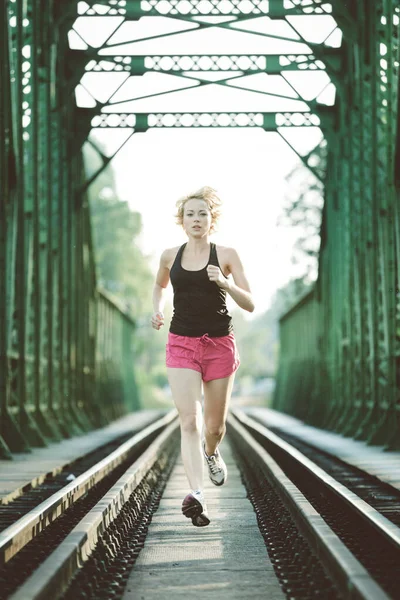 Athlete running on railaway bridge training for marathon and fitness. Healthy sporty caucasian woman exercising in urban environment before going to work. Active urban lifestyle — Stock Photo, Image