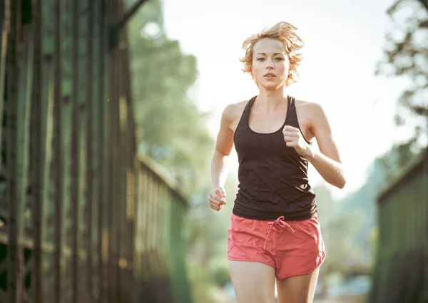 Atleta corriendo en el entrenamiento del puente ferroviario para maratón y fitness. Mujer sana deportiva caucásica haciendo ejercicio en el entorno urbano antes de ir a trabajar. Estilo de vida urbano activo —  Fotos de Stock