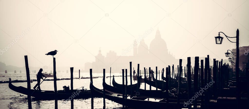 Romantic Italian city of Venice, a World Heritage Site: traditional Venetian wooden boats, gondolier and Roman Catholic church Basilica di Santa Maria della Salute in the misty background