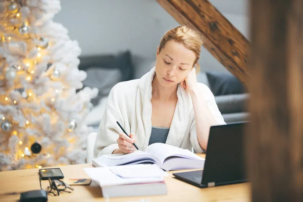 Die junge Unternehmerin im kuschelig warmen Bademantel arbeitet während der Coronavirus-Pandemie im Jahr 2020 von zu Hause aus. Arbeit von zu Hause aus, selter an Ort und Stelle, Konzept. — Stockfoto