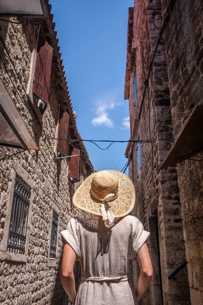 Achteraanzicht van mooie blonde jonge vrouwelijke reiziger met strohoed sightseeing en genieten van de zomervakantie in een oude traditionele kustplaats aan de Adriatische kust kosten, Kroatië — Stockfoto