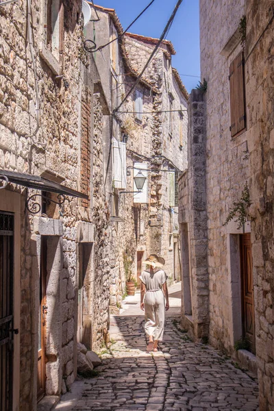 Rear view of beautiful blonde young female traveler wearing straw sun hat sightseeing and enjoying summer vacation in an old traditional costal town at Adriatic cost, Croatia — Stock Photo, Image