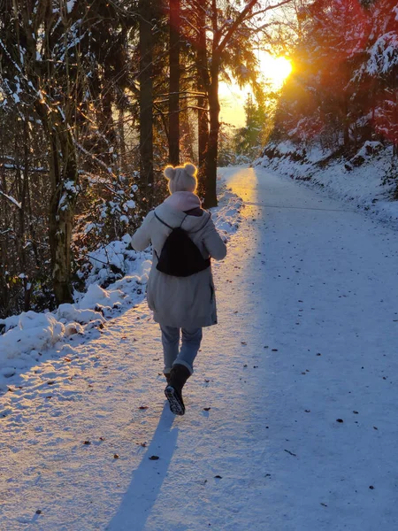 Vrouw wandelend op sneeuw in het witte winterwoud droeg de zonsondergang. Recreatie en gezonde levensstijl buiten in de natuur — Stockfoto