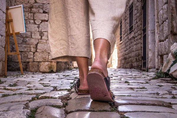 Detail shot of female legs wearing comfortable travel sandals walking on old medieval cobblestones street dring sightseeing city tour. Travel, tourism and adventure concept — Stock Photo, Image