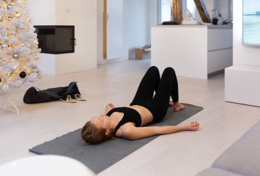 Güzel sarışın kadın evde antrenman yapıyor. Kadın evde yoga yapıyor. Sağlıklı ve aktif yaşam tarzı için egzersiz dersleri alan formda bir kız. Kadın ev işleri için karantina kullanıyor.