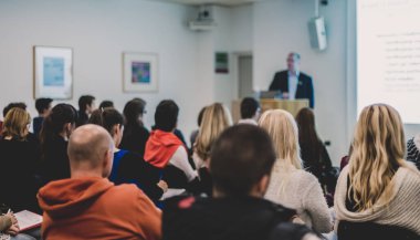 Üniversitedeki konferans salonunda sunum yapan adam.