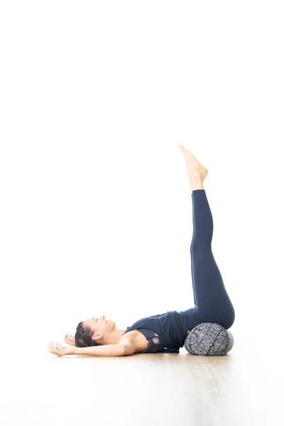 Joga odtwórcza ze wzmacniaczem. Młoda, sportowa, atrakcyjna kobieta w jasnobiałej pracowni jogi, leżąca na poduszce, rozciągająca się i relaksująca podczas jogi odtwórczej. Zdrowy aktywny tryb życia — Zdjęcie stockowe