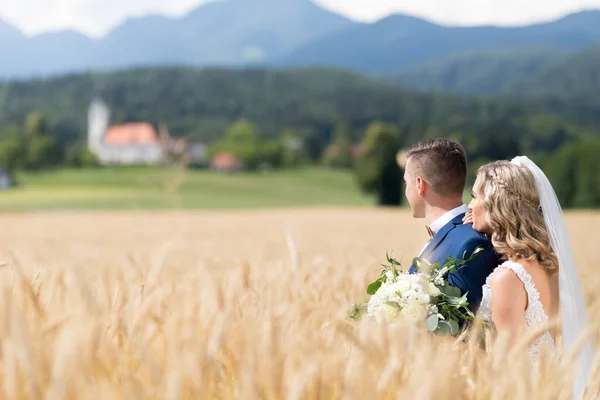 Νύφη αγκαλιάζει τον γαμπρό τρυφερά σε χωράφι με σιτάρι κάπου στη σλοβενική ύπαιθρο. — Φωτογραφία Αρχείου