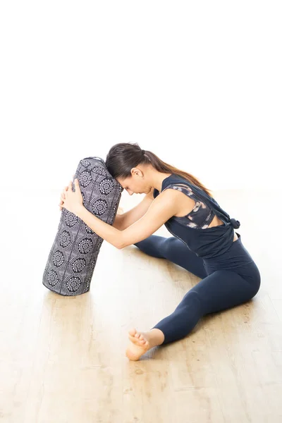 Yoga restaurativo con refuerzo. Joven mujer atractiva deportiva en estudio de yoga blanco brillante, acostada en cojín de refuerzo, estirándose y relajándose durante el yoga restaurativo. Vida activa saludable —  Fotos de Stock