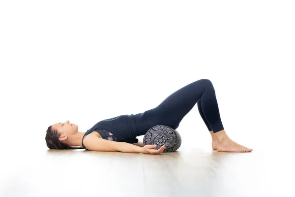 Återställande yoga med en bolster. Ung sportig attraktiv kvinna i ljus vit yogastudio, liggande på bolsterkudde, stretching och avkoppling under stärkande yoga. Hälsosam aktiv livsstil — Stockfoto