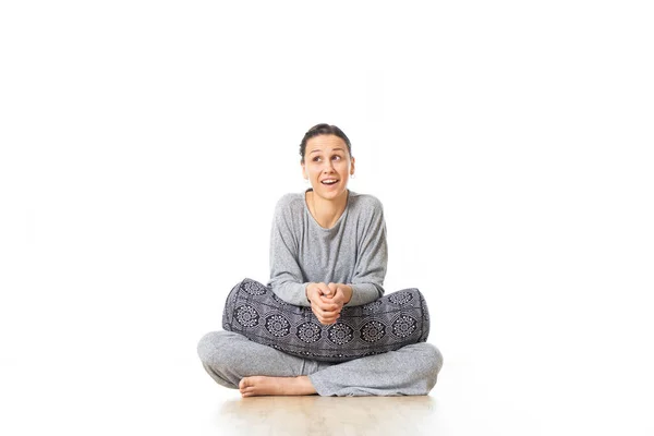 Yoga restaurador com um reforço. Jovem desportivo feminino instrutor de ioga sentado no estúdio de ioga branco brilhante segurando almofada de reforço mostrando amor e paixão por ioga restaurador — Fotografia de Stock