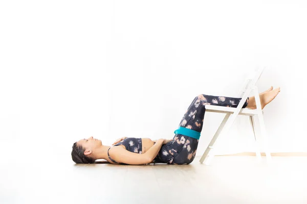 Joven mujer atractiva deportiva en estudio de yoga blanco brillante, estirándose y relajándose durante el yoga restaurativo utilizando silla blanca como gadget. Vida activa saludable —  Fotos de Stock