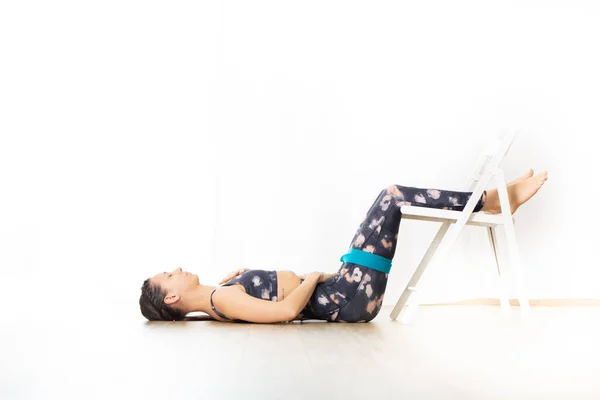 Young sporty attractive woman in bright white yoga studio, stretching and relaxing during restorative yoga using white chair as a gadget. Healthy active lifestyle — Stock Photo, Image