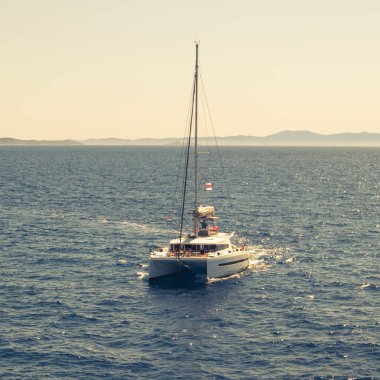 Çift katlı bir katamaran, yelkenleri açık bir yat, ufka doğru bakıyor. Hırvatistan açıklarında güneşli bir günde masmavi okyanus