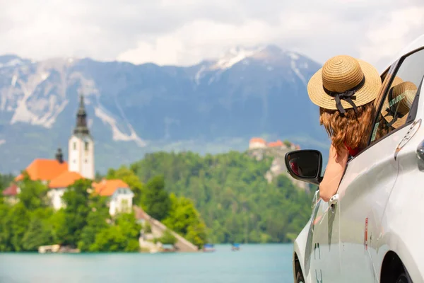 Glückliche junge Frau im Urlaub lehnt sich aus dem Autofenster am Ufer des Bleder Sees in Slowenien. Reisen, Urlaub, Tourismus, erkunden, Auto mieten. — Stockfoto