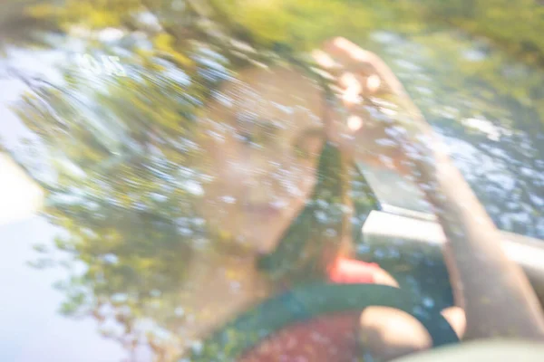 Beweging wazig beeld van gelukkige jonge vrouw rijden een auto op een zomer road trip reizen vakanties. Schot door de voorruit. — Stockfoto