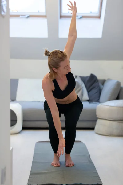 Hermosa mujer rubia haciendo ejercicio en casa en interiores. Las mujeres practican yoga en casa. Chica en forma usando tutoriales de entrenamiento para un estilo de vida activo saludable. Mujer que usa cuarentena para entrenamientos en casa. — Foto de Stock