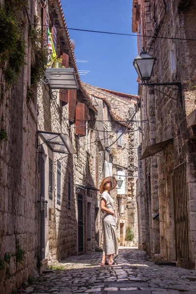 Beautiful blonde young female traveler wearing straw sun hat sightseeing and enjoying summer vacation in an old traditional costal town at Adriatic cost, Croatia. — Stock Photo, Image