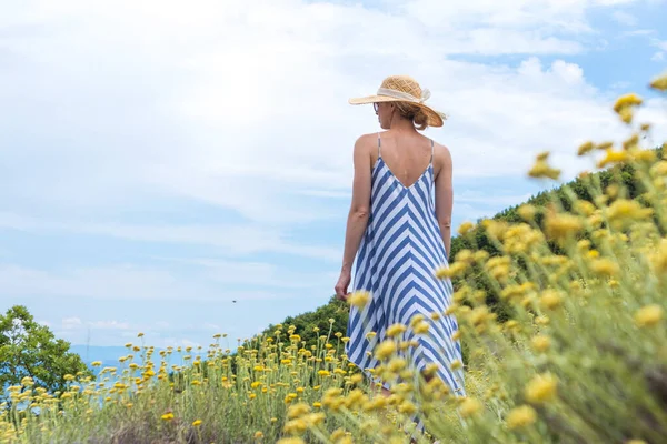 Ung kvinna bär randig sommar klänning och halm hatt stående i super blomning av vilda blommor, avkopplande och samtidigt enjoing vacker natur Adriatiska havet kust natur Kroatien. — Stockfoto