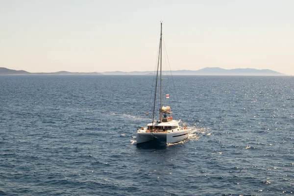 Dubbeldäckad katamaran, en yacht med sänkta segel, blickar mot horisonten. Det azurblå havet en solig dag utanför Kroatiens kust — Stockfoto