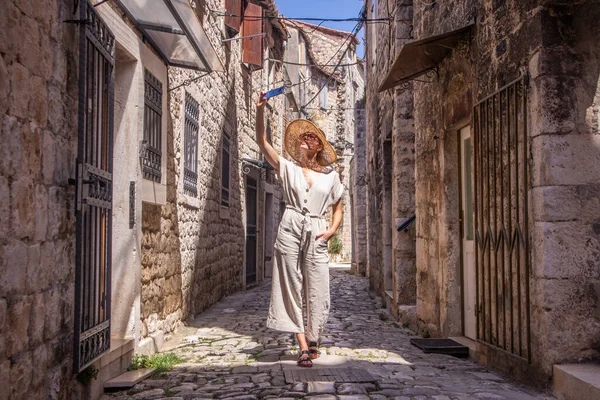 Schöne blonde junge Reisende mit Strohsonnenhut, Selfie beim Sightseeing und genießen den Sommerurlaub in einer alten traditionellen Küstenstadt an der Adria, Kroatien. — Stockfoto