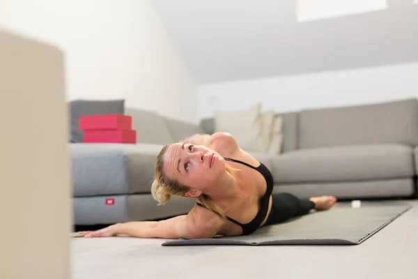 Hermosa mujer rubia haciendo ejercicio en casa en interiores. Las mujeres practican yoga en casa. Chica en forma usando tutoriales de entrenamiento para un estilo de vida activo saludable. Mujer que usa cuarentena para entrenamientos en casa. — Foto de Stock