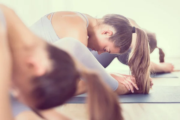 Groep van jonge sportieve aantrekkelijke vrouwen in yoga studio, het beoefenen van yoga les met instructeur, zitten op de vloer in voorwaartse buiging yoga sana houding. Gezonde actieve levensstijl, sporten in de fitnessruimte — Stockfoto