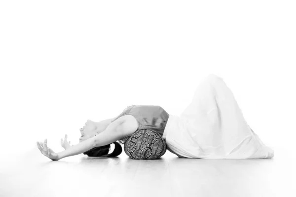 Yoga ristoratore con un sostenitore. Giovane donna attraente sportiva in luminoso studio di yoga bianco, stretching e rilassante durante lo yoga ristoratore con cuscino di rinforzo. Stile di vita sano e attivo — Foto Stock