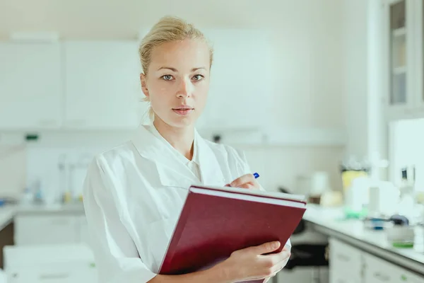 Portrait of young, confident female health care professional taking notes during inventory in scientific laboratory or medical doctors office — Stock Photo, Image