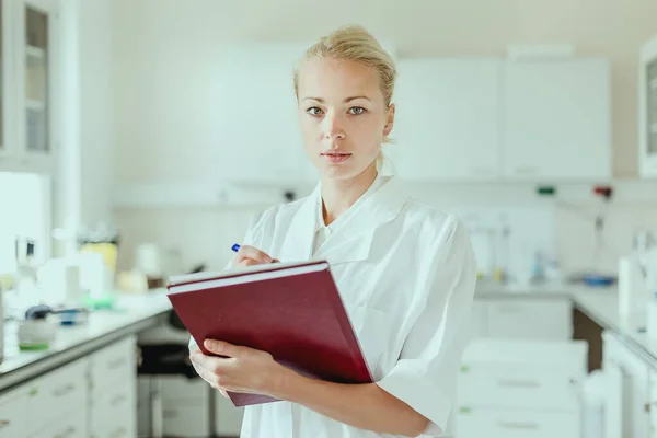 Portrait of young, confident female health care professional taking notes during inventory in scientific laboratory or medical doctors office — Stock Photo, Image