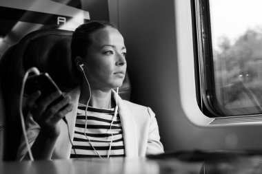 Trenle seyahat ederken cep telefonundan podcast dinleyen düşünceli iş kadını..
