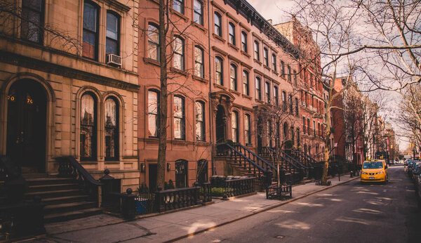 Row of old brownstone buildings along an empty sidewalk block in the Greenwich Village neighborhood of Manhattan, New York City, NYC, USA.