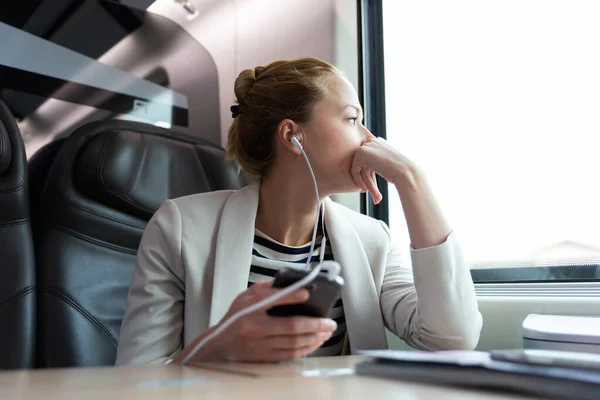 Omtänksam affärskvinna lyssnar på podcast på mobiltelefon när du reser med tåg. — Stockfoto