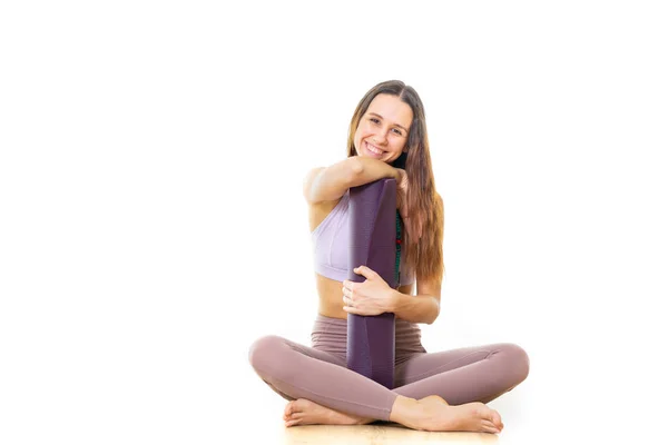Jeune instructrice de yoga sportive dans un studio de yoga blanc brillant, tenant un tapis de yoga, souriant, regardant la caméra — Photo