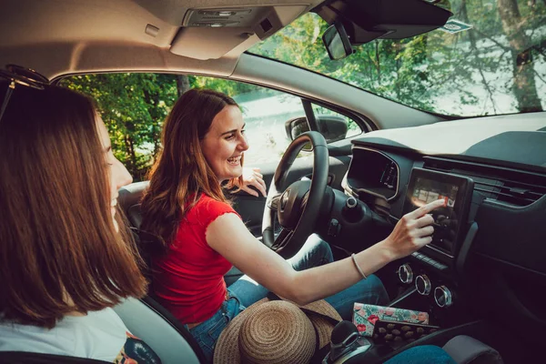 Dos jóvenes amigas conduciendo, escuchando buena música en coche, disfrutan de un viaje por carretera en verano. —  Fotos de Stock