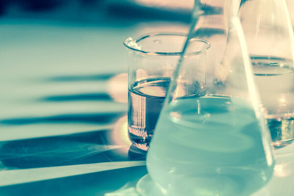 Illuminated laboratory flask filed with colorful chemical solutions with shadows on the table. Laboratory, science, chemistry... consept.