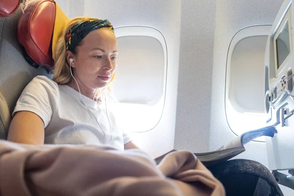 Mujer joven ocasional leyendo revista y escuchando música en el avión. Mujer viajera leyendo sentada en cabina de pasajero. — Foto de Stock