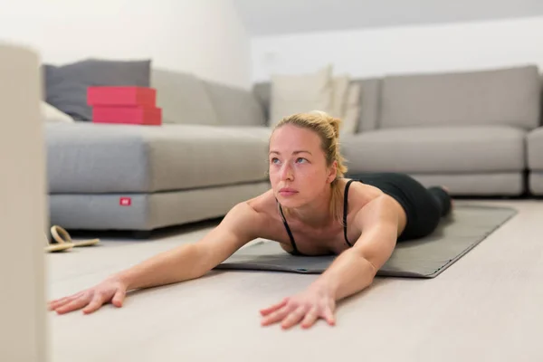 Hermosa mujer rubia haciendo ejercicio en casa en interiores. Las mujeres practican yoga en casa. Chica en forma usando tutoriales de entrenamiento para un estilo de vida activo saludable. Mujer que usa cuarentena para entrenamientos en casa. — Foto de Stock