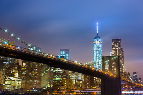 Brooklyn bridge and New York City Manhattan downtown skyline at dusk with skyscrapers illuminated over East River panorama.