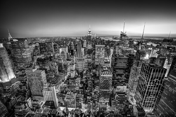 New York City. Manhattan downtown skyline with illuminated Empire State Building and skyscrapers at dusk seen from Top of the Rock observation deck. Black and white shot.