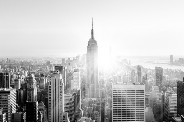 New York City. Manhattan downtown skyline with illuminated Empire State Building and skyscrapers at sunset. Vertical composition. Sunbeams and lens flare. Black and white image.