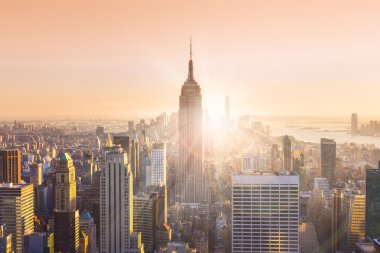 New York şehri. Işıklı Empire State Binası ve gün batımında gökdelenler ile Manhattan şehir silueti. Yatay kompozisyon. Sıcak akşam renkleri. Güneş ışınları ve mercek parlaması.