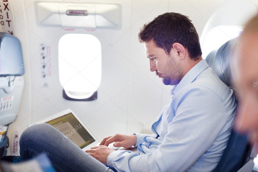 Businessman working with laptop on airplane.