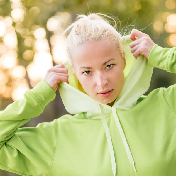 Selbstbewusste, sportliche Frau im modischen grünen Kapuzenpulli. — Stockfoto