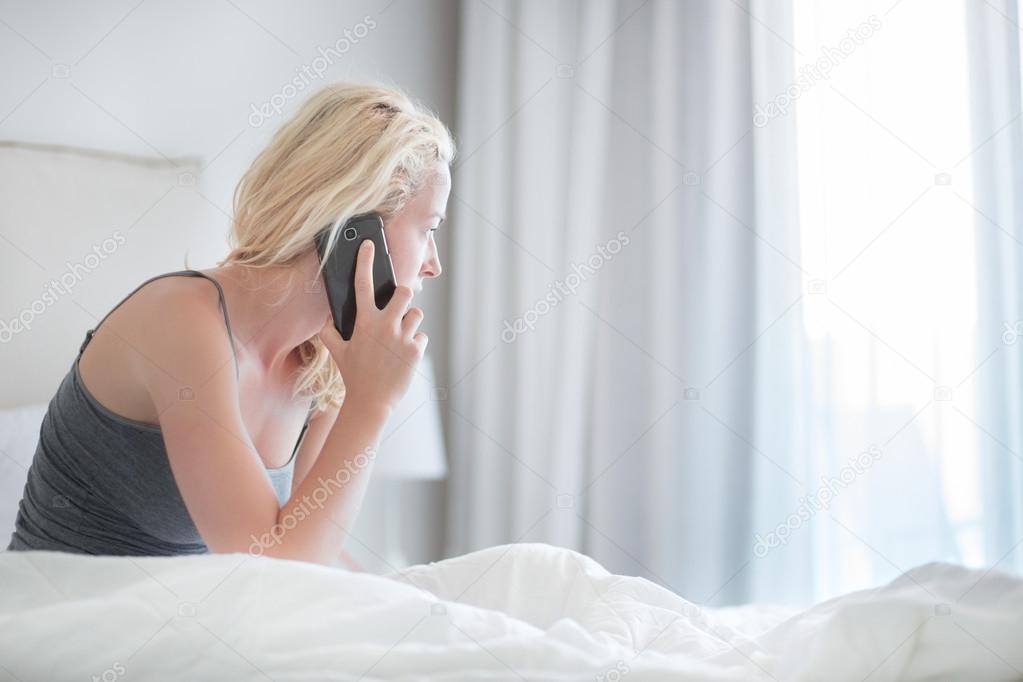 Woman talking by phone on bed in morning.