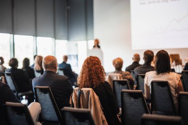 İş ve girişimcilik sempozyumu. İş toplantısında kadın konuşmacı bir konuşma yapıyor. Konferans salonunda dinleyiciler. İzleyicilerin tanınmayan katılımcılarının arka görünümü.