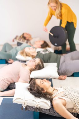 Tibet davuluyla grup terapisi. Etrafı bakır kaselerle çevrili bir grup kadın için ahşap zeminde yatıyorlar. Meditasyon ve rahatlama