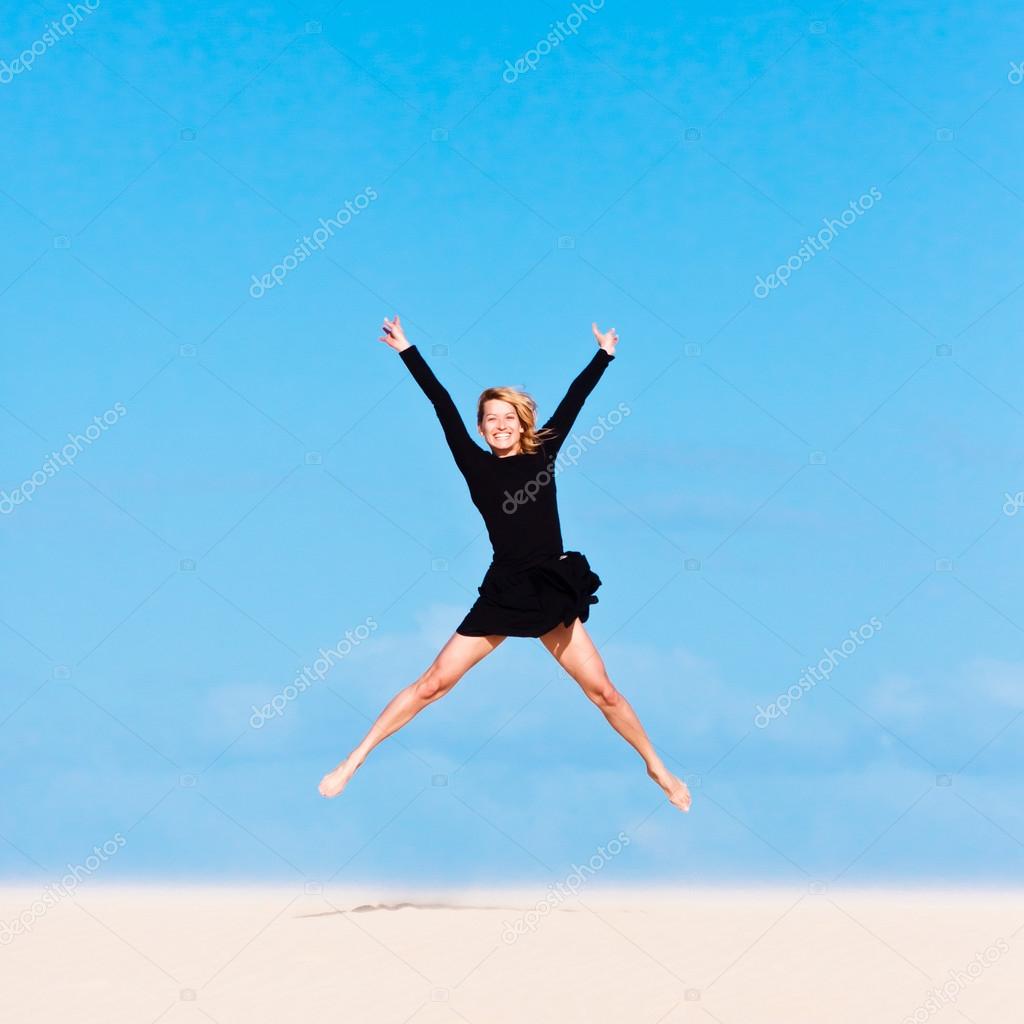 Girl jumping in the air on sand dune.