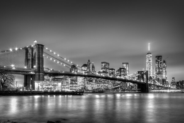 Brooklyn bridge and New York City Manhattan downtown skyline at dusk with skyscrapers illuminated over East River panorama. Copy space. Black and white image.