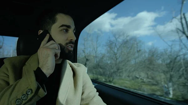 Young guy sitting in the car. A business man sits in a car talk with phone and looks out of the window at the winter landscapes. Photo, still, image.